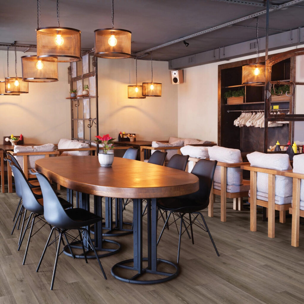 COREtec luxury vinyl floorind in a commercial dining room and bar space with a large, wooden table, modern chaits, and antique looking light fixtures