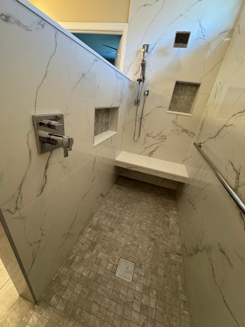 smooth marble tile in a walk-in shower with cubby holes, grab bars and a shower seat
